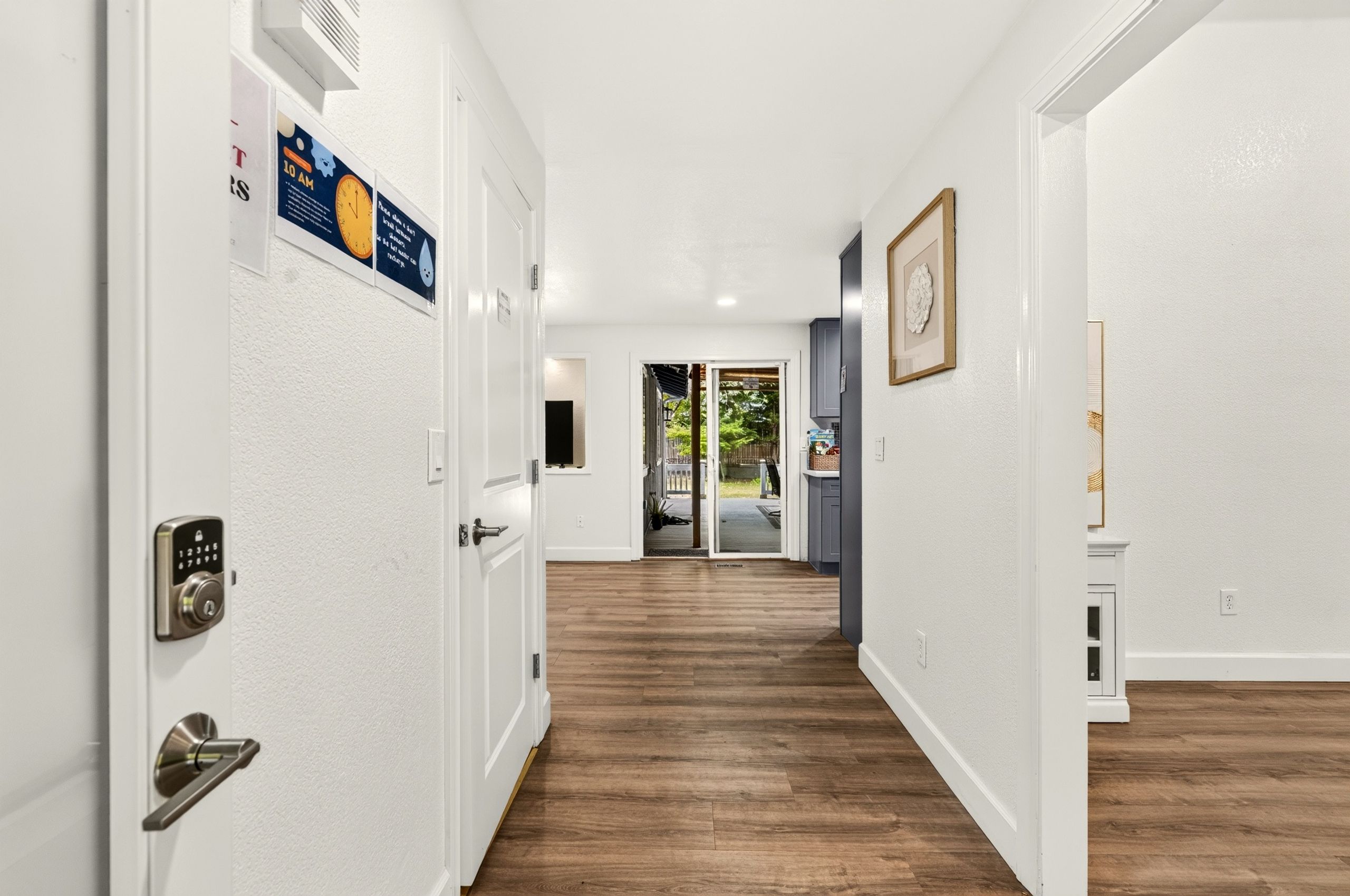 Un pasillo con piso de madera, paredes blancas y una puerta con cerradura electrónica.