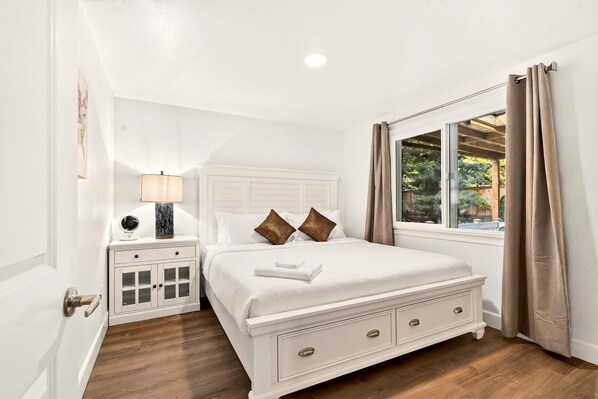 A bedroom with a bed, bedside table, lamp, and window with curtains.