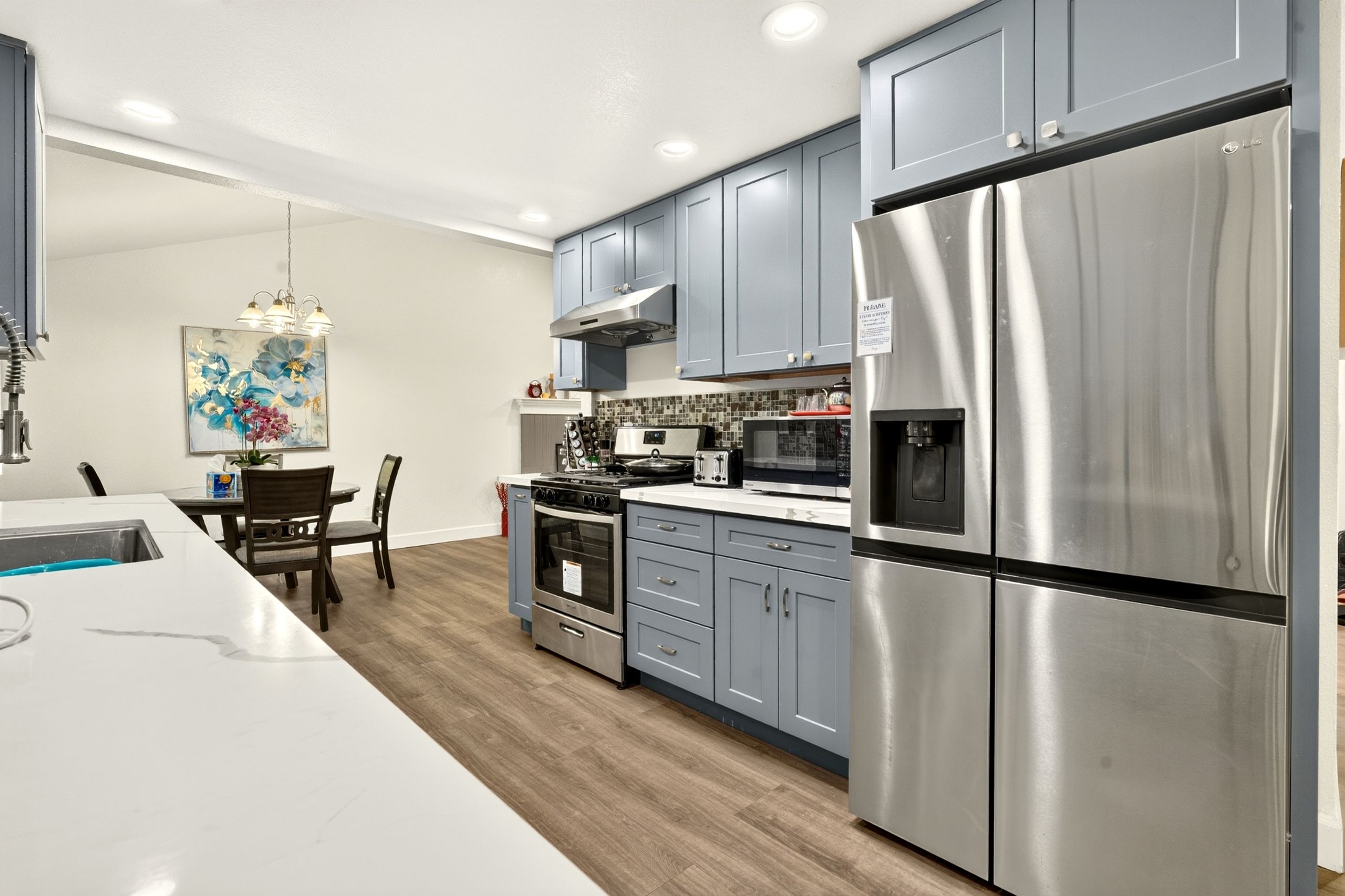 A modern kitchen with stainless steel appliances, a dining area with a table and chairs, and a decorative painting on the wall.