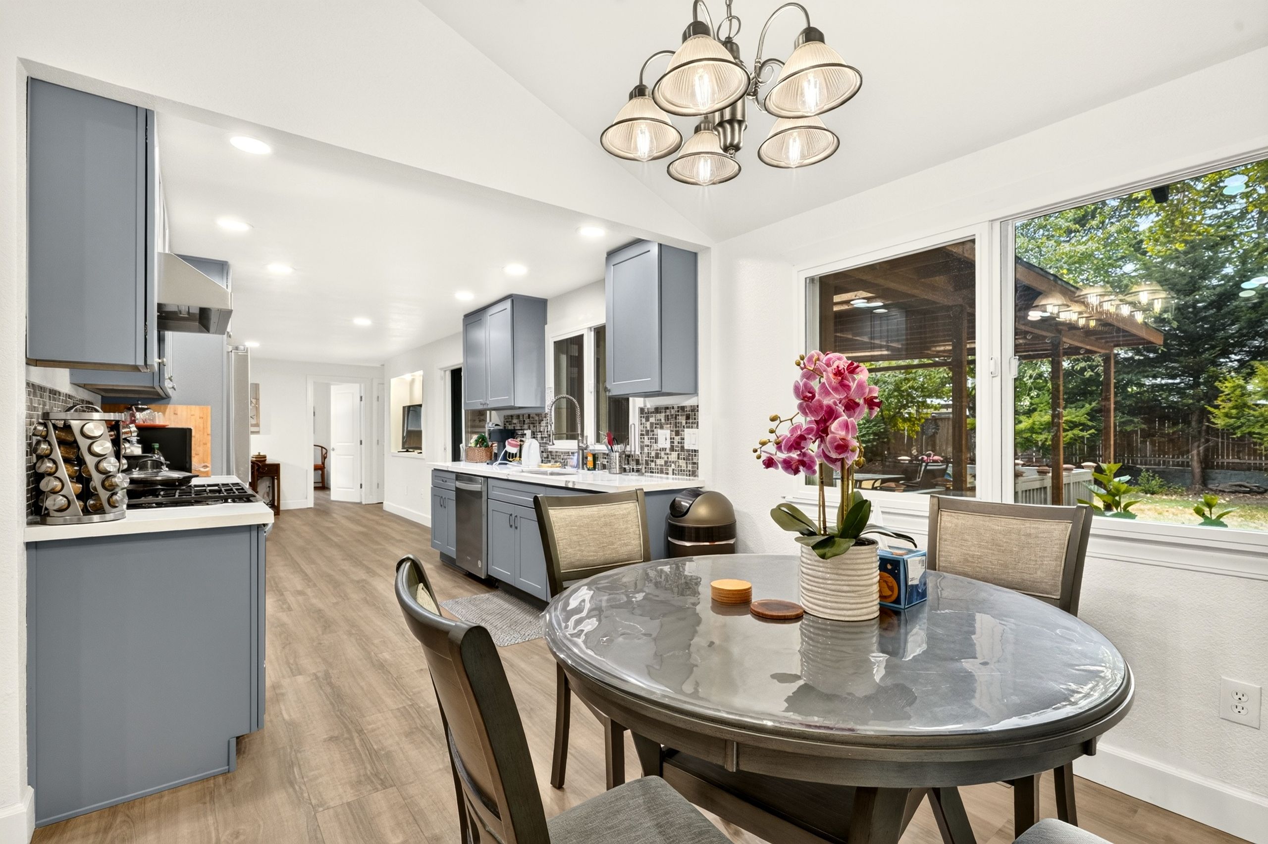 A modern kitchen with grey cabinets, a central island, and a dining area with a glass table.