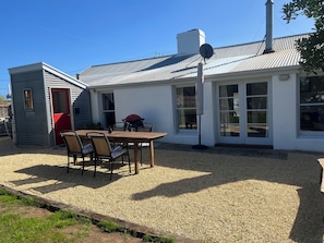 Ein Haus mit Kiesterrasse, einem Esstisch mit Stühlen, einem Grill und einer Satellitenschüssel.