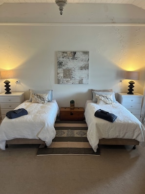 Ein Schlafzimmer mit zwei Betten, einem Teppich, einer Holzkiste und einem Wandbild.