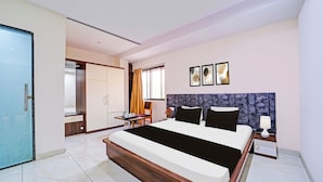 A modern hotel room with a large bed, a bedside table, a nightstand, a window with curtains, and a door. - Townhouse LIG Main Road Indore (Indore)