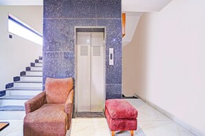 An elevator with a control panel, a staircase with alternating dark and light steps, and two upholstered chairs. - Townhouse LIG Main Road Indore (Indore)