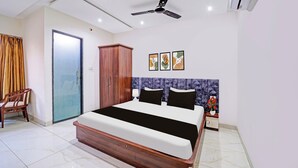 A hotel room with a bed, a wardrobe, a chair, a ceiling fan, and a wall-mounted air conditioner. - Townhouse LIG Main Road Indore (Indore)