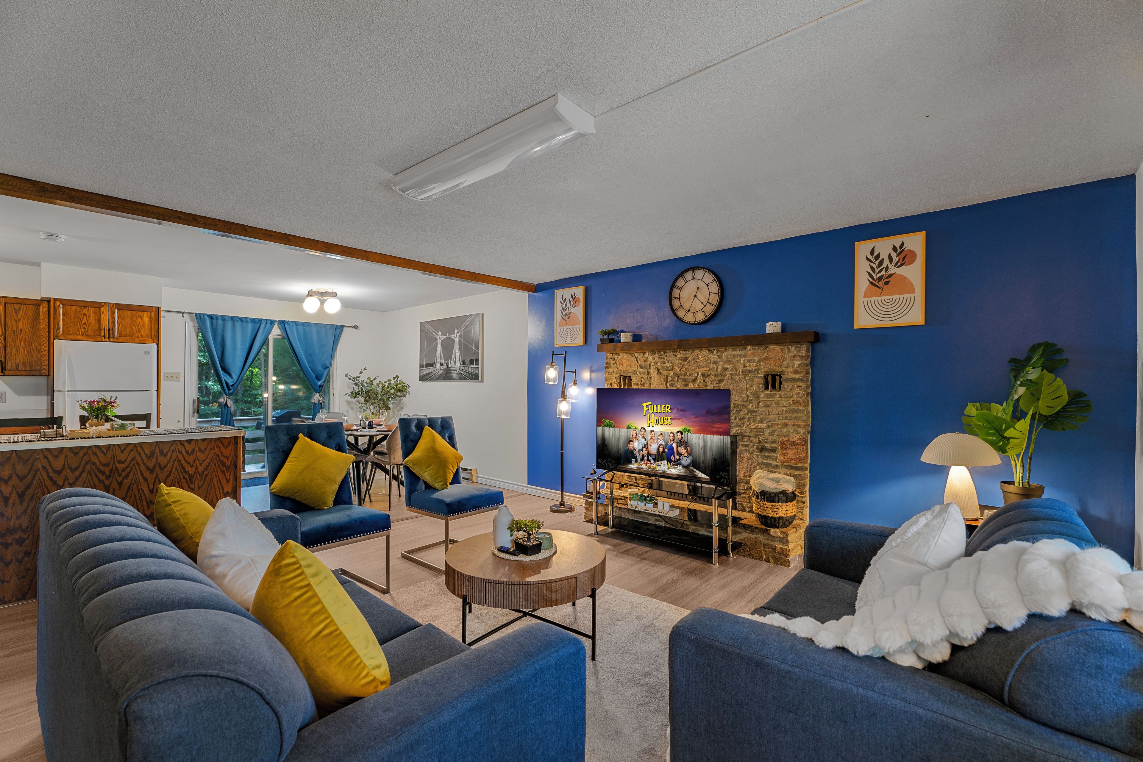 Una sala de estar con chimenea, paredes azules y una cocina al fondo.