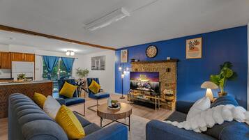 Una sala de estar con chimenea, paredes azules y una cocina al fondo.