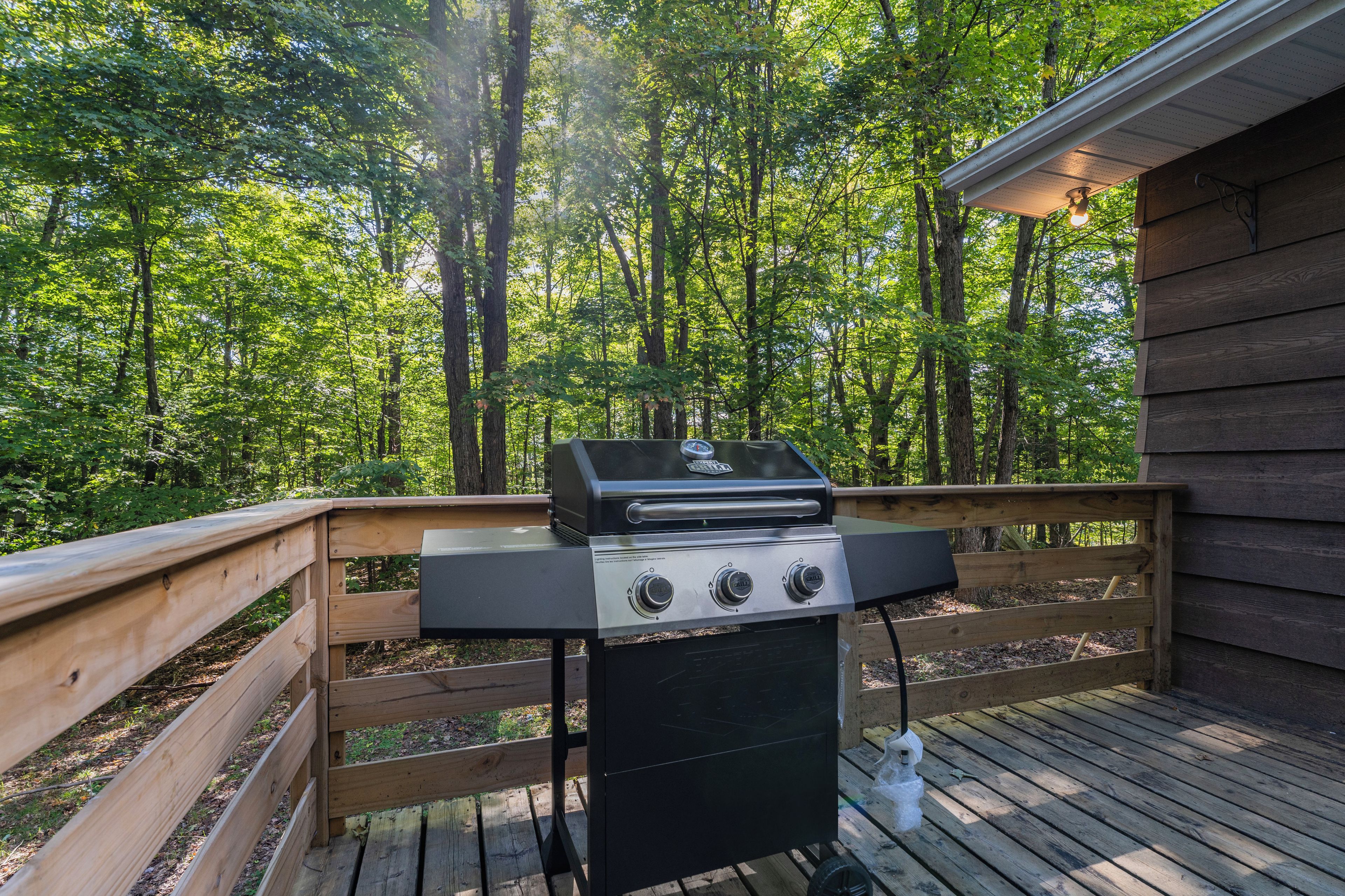 Ein Grill auf einer Holzterrasse mit Wald im Hintergrund.