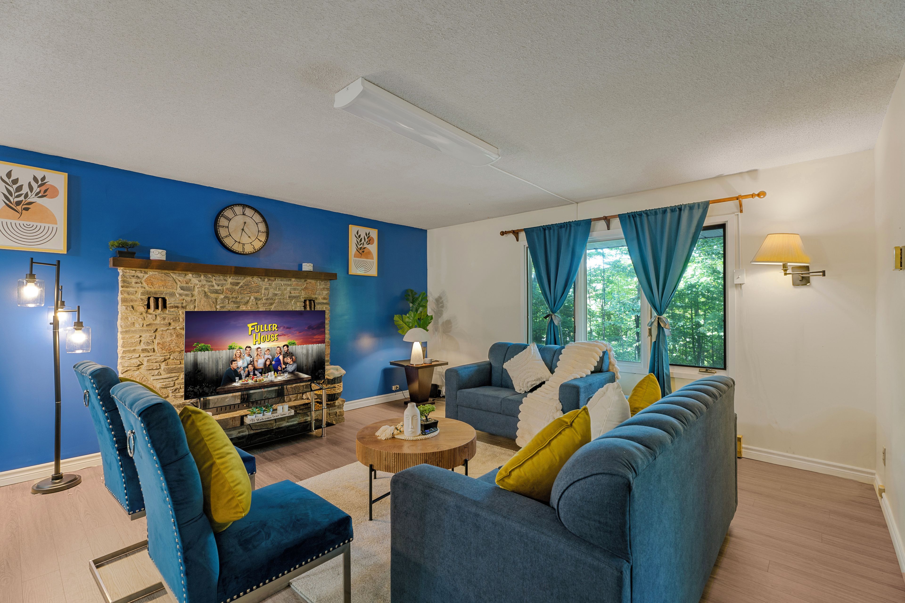 Ein Wohnzimmer mit Kamin aus Stein, blauen Wänden, einer Uhr und einem Sofa mit Kissen.