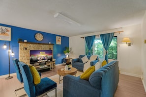 A living room with a stone fireplace, blue walls, a clock, and a sofa with cushions. - Huntsville Retreat with Fire Pit, BBQ • Near Downtown (Huntsville)