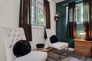 A room with two white tufted chairs, a wooden side table with a lamp, and a small shelf with decorative items. - Huntsville Retreat with Fire Pit, BBQ • Near Downtown (Huntsville)