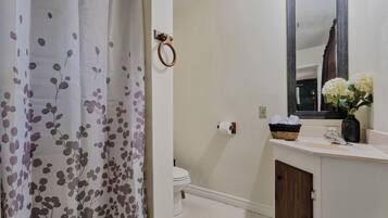 A bathroom with a toilet, a sink with a mirror, a shower curtain, and a vase with flowers on the sink.