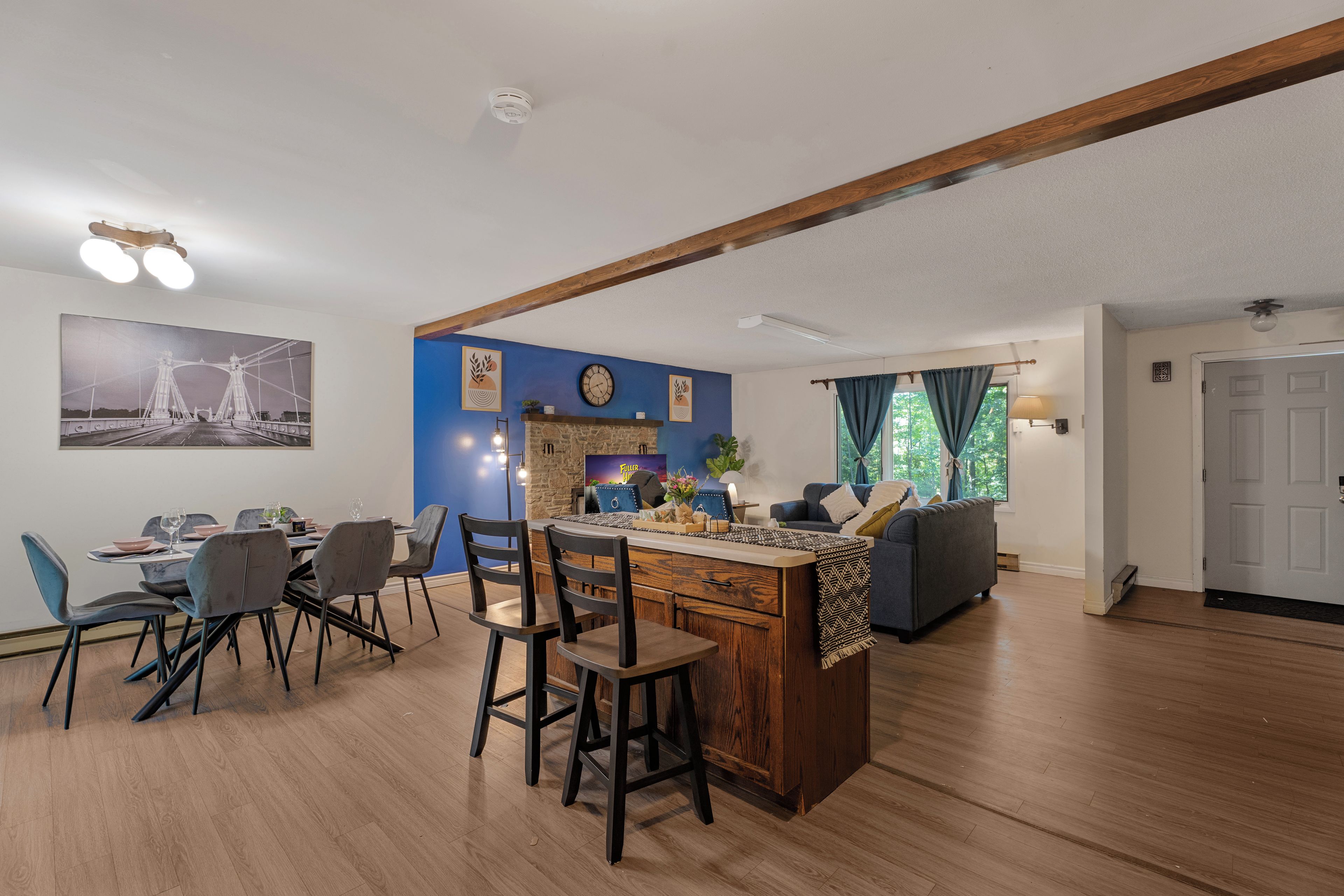 A modern kitchen with a central island, dining area with chairs, and a living room with a sofa and a TV.