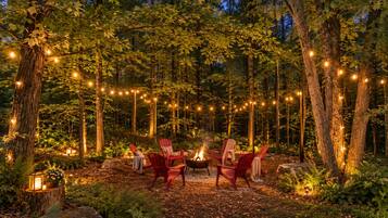 A forest setting with a fire pit and red chairs arranged for seating.