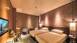 Habitación de hotel con dos camas, televisión, escritorio con lámpara y vista al exterior.