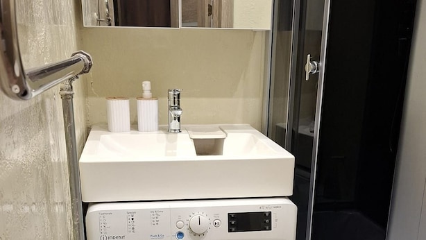 Un baño pequeño equipado con lavadora, lavamanos y ducha.