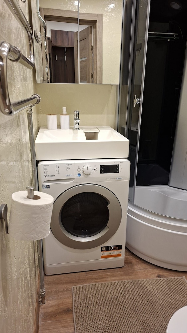 Ein kleines Badezimmer mit Waschmaschine, Waschbecken und Dusche.