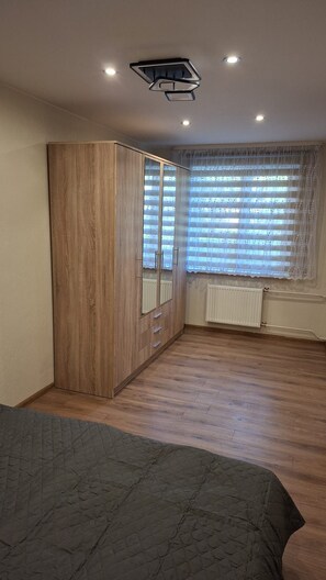A bedroom with a wardrobe, a radiator, and a window with blinds.