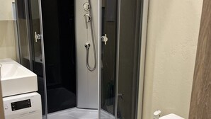 Un baño compacto con ducha envuelta en vidrio, inodoro y lavadora.