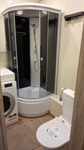Ein kleines Badezimmer mit einer Duschkabine, Toilette und Waschmaschine.