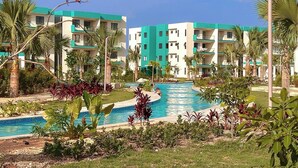 A resort with a central swimming pool surrounded by lush greenery and multi-story buildings with balconies. - Serena Village | Pool, balcony, and near PUJ (Punta Cana)