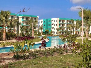 Un resort con una piscina central rodeada de exuberante vegetación y edificios de varios pisos con balcones.