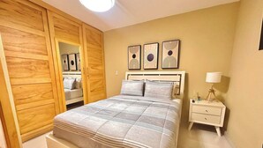 A bedroom with a bed, a nightstand, a lamp, a wardrobe, and three wall art pieces. - Serena Village | Pool, balcony, and near PUJ (Punta Cana)