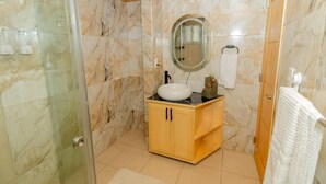 A bathroom with a glass shower enclosure, a wooden vanity with a white sink, and a marble-tiled wall. - Serena Village | Pool, balcony, and near PUJ (Punta Cana)