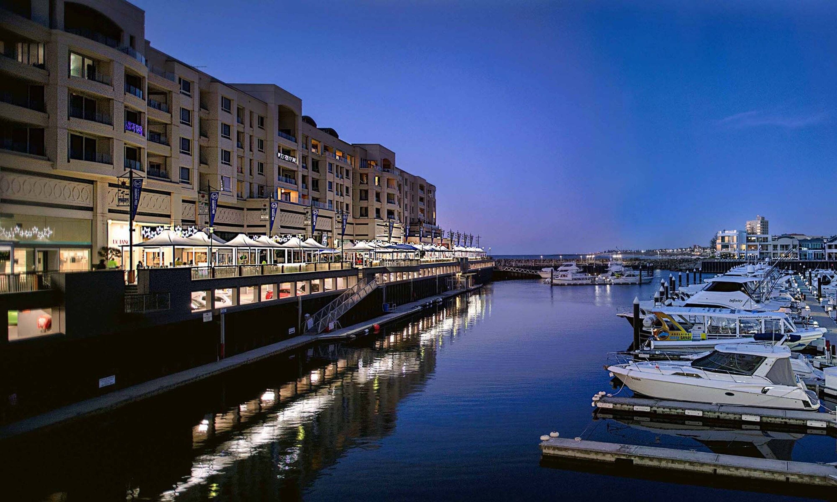 A waterfront hotel with multiple balconies, a marina with boats, and outdoor seating areas.