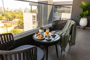 A balcony with a table set for breakfast, including croissants, fruit, and orange juice.