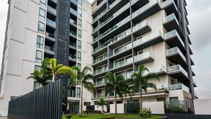 A modern multi-story building with balconies, a landscaped courtyard, and a black vertical structure.