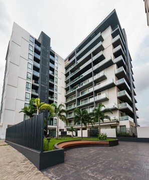 A modern multi-story building with balconies, a landscaped courtyard, and a black vertical structure.