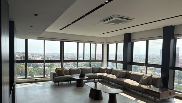 A spacious living area with a large sectional sofa, two round coffee tables, and a city view through expansive windows.