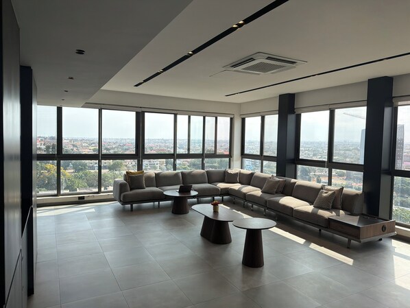 A spacious living area with a large sectional sofa, two round coffee tables, and a city view through expansive windows.