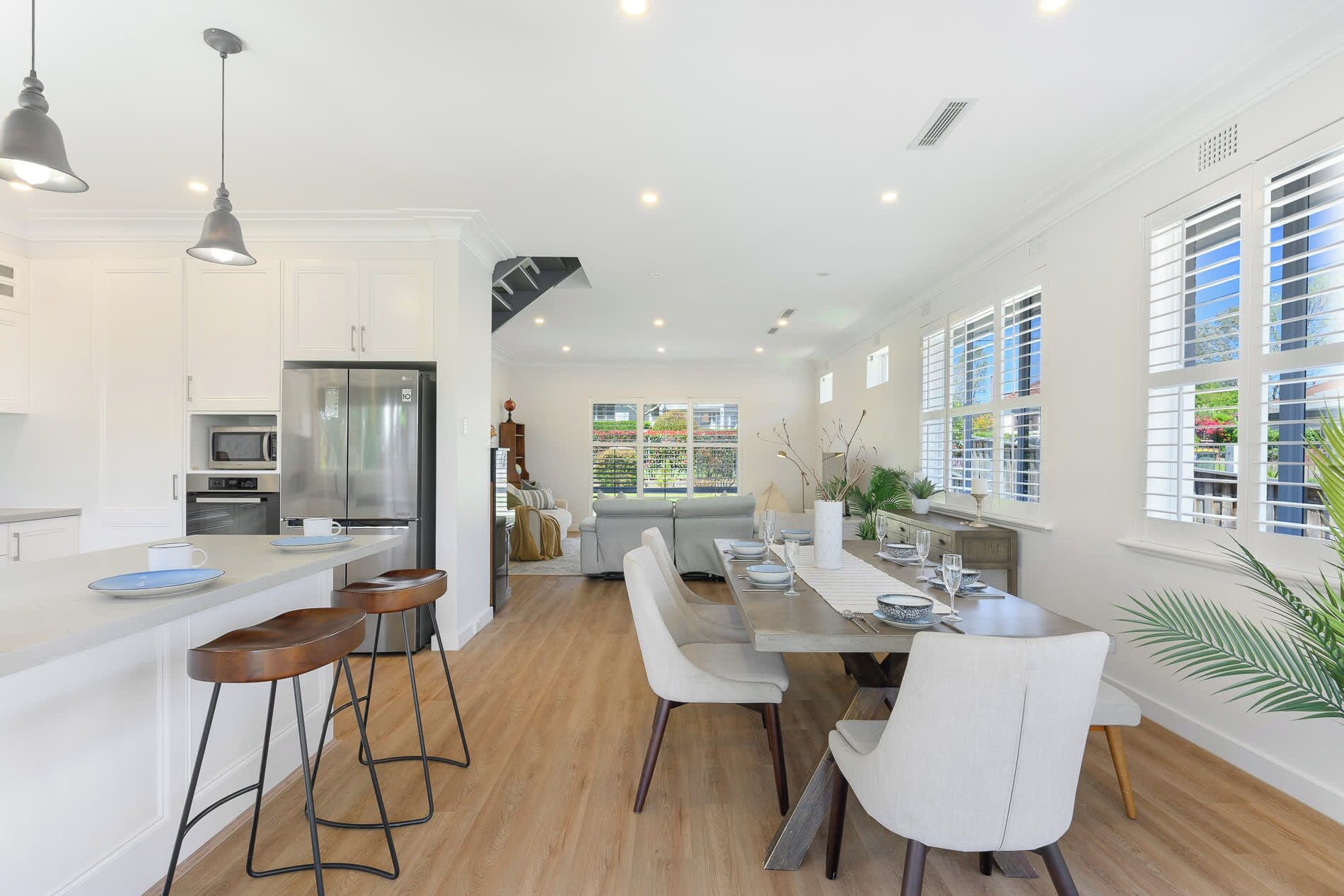 A modern kitchen with a central island, bar stools, and a dining area with a long table and chairs.