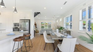 A modern kitchen with a central island, bar stools, and a dining area with a long table and chairs. - Cosy 3 bedrooms Lane Cove 10 Mins to Sydney CBD (Lane Cove North)
