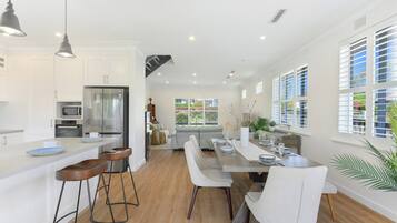 A modern kitchen with a central island, bar stools, and a dining area with a long table and chairs.