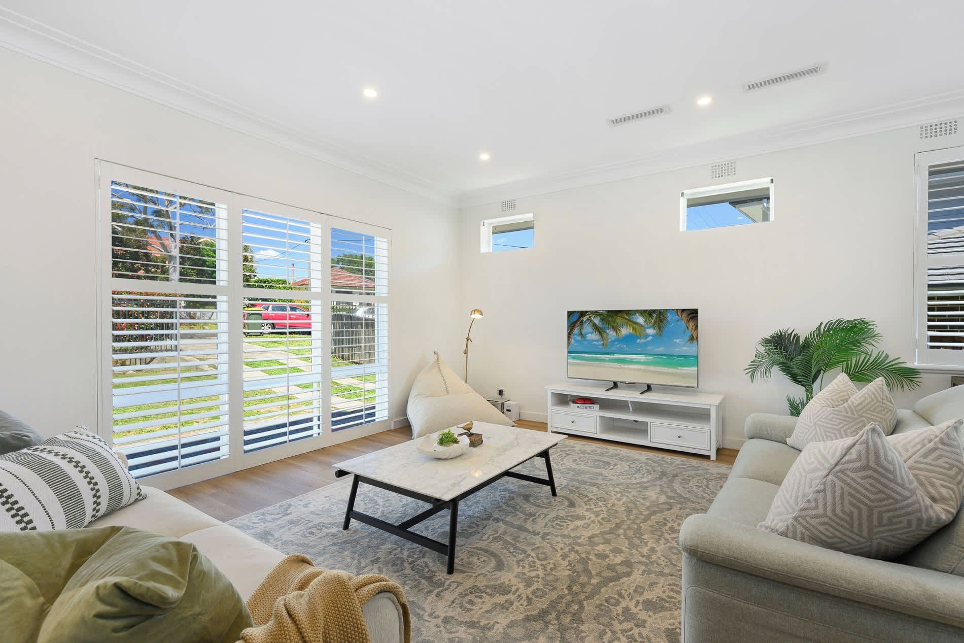 A living room with a sofa, a coffee table, a TV, and a large window with blinds.