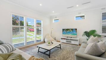 A living room with a sofa, a coffee table, a TV, and a large window with blinds.