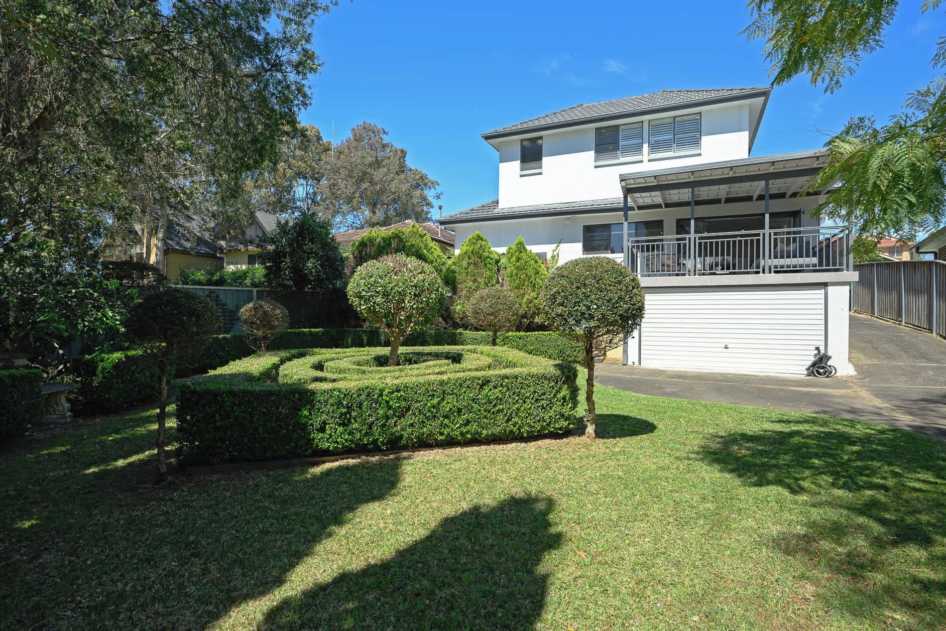 A modern two-story house with a garage, surrounded by well-maintained hedges and trees.