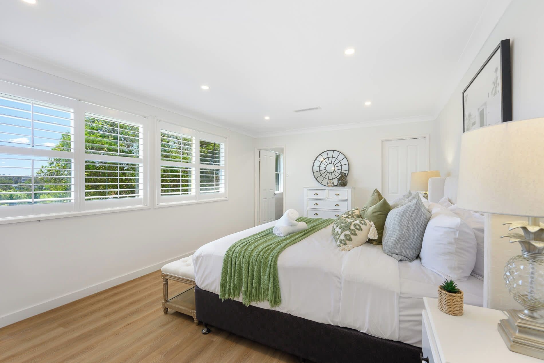 A bedroom with a bed, a dresser, a mirror, and a window with blinds.