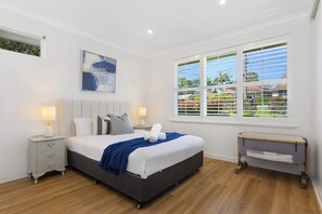 Quarto com cama, mesas de cabeceira, venezianas na janela e vista para o verde lá fora.
