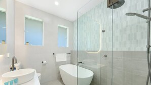 A modern bathroom with a freestanding bathtub, a glass-enclosed shower, and a vanity with a sink and toiletries. - Cosy 3 bedrooms Lane Cove 10 Mins to Sydney CBD (Lane Cove North)