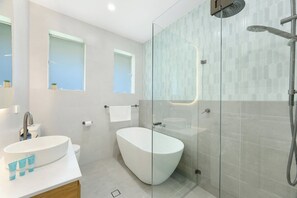 Een moderne badkamer met een vrijstaand bad, een douche met glazen wanden en een wastafel met zeep en toiletartikelen.