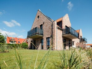 Ein modernes, zweistöckiges Haus aus Backstein mit Balkonen und einem gepflegten Rasen.