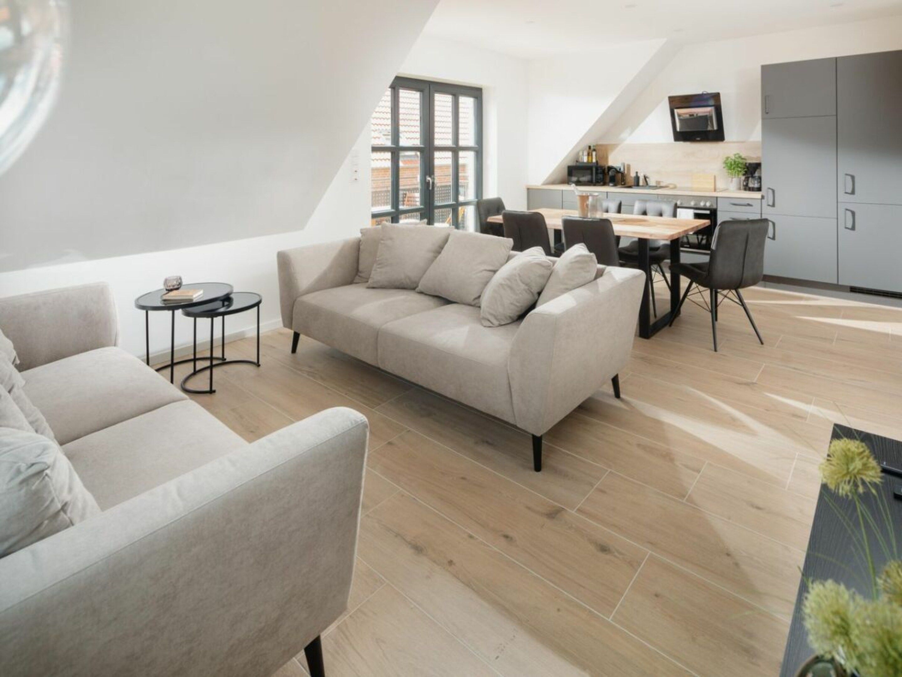 A modern living room with a sofa and chairs, a dining area with a table and chairs, and a kitchen with cabinets and a TV.