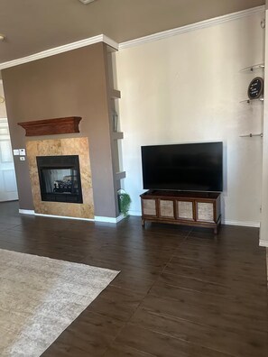 Una sala de estar con chimenea, un televisor de pantalla plana sobre un soporte de madera y un tapete grande.