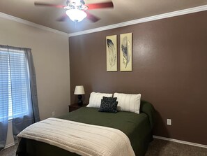 A bedroom with a bed, a ceiling fan, a window with blinds, and two wall-mounted paintings. - Soothing 3-bedroom house with AC in charming Lawton (Lawton)