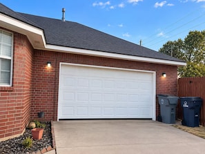 A residential garage with a white garage door, a brick exterior, and two trash bins labeled 'Lawton' beside it. - Soothing 3-bedroom house with AC in charming Lawton (Lawton)