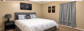 Un dormitorio con cama, mesita de noche, lámpara y dos cuadros colgados en la pared.